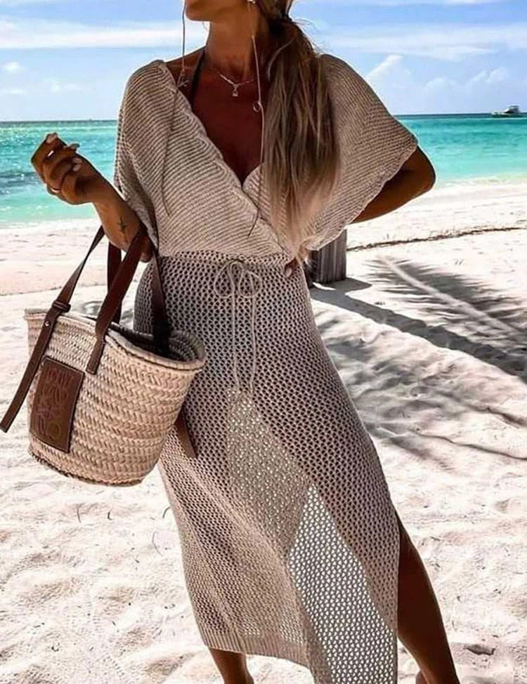 Donna in spiaggia con abito crochet beige, borsa di paglia, mare turchese sullo sfondo. Moda estiva, abbigliamento da spiaggia elegante.
