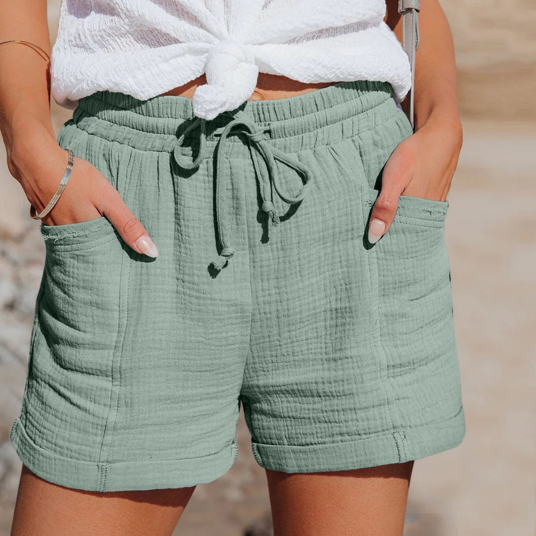 Shorts estivi verdi in cotone, con tasche e laccio in vita, indossati da una donna. Abbigliamento casual da spiaggia, moda estiva femminile.