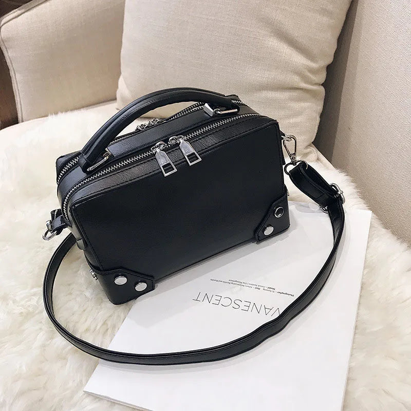 Borsa a tracolla nera in pelle su sedia beige, design elegante con doppia zip e manico superiore, ideale per moda donna e accessori di lusso.