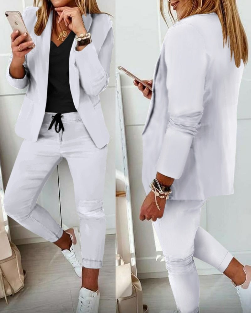 Donna in abito bianco casual, giacca e pantaloni, con smartphone. Look moderno e chic, perfetto per ufficio o eventi informali.