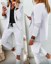 Donna in abito bianco casual, giacca e pantaloni, con smartphone. Look moderno e chic, perfetto per ufficio o eventi informali.