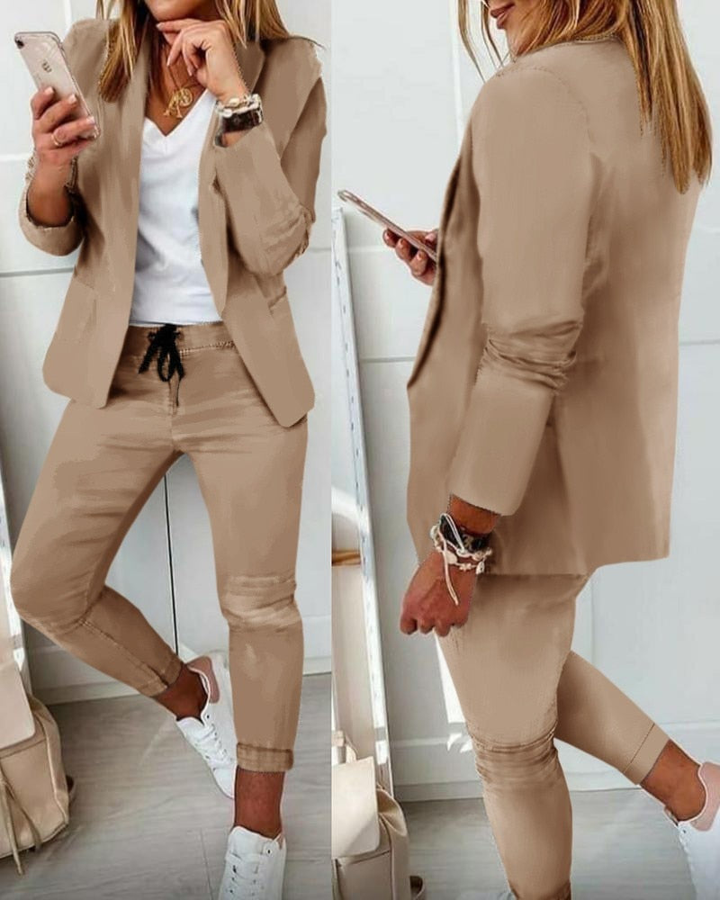 Completo donna beige elegante, giacca e pantaloni, abbinato a t-shirt bianca e sneakers. Moda casual chic, outfit primaverile.