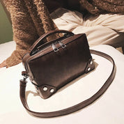 Borsa a tracolla in pelle marrone su letto, design elegante con manico superiore e dettagli metallici. Accessorio moda donna, stile casual chic.