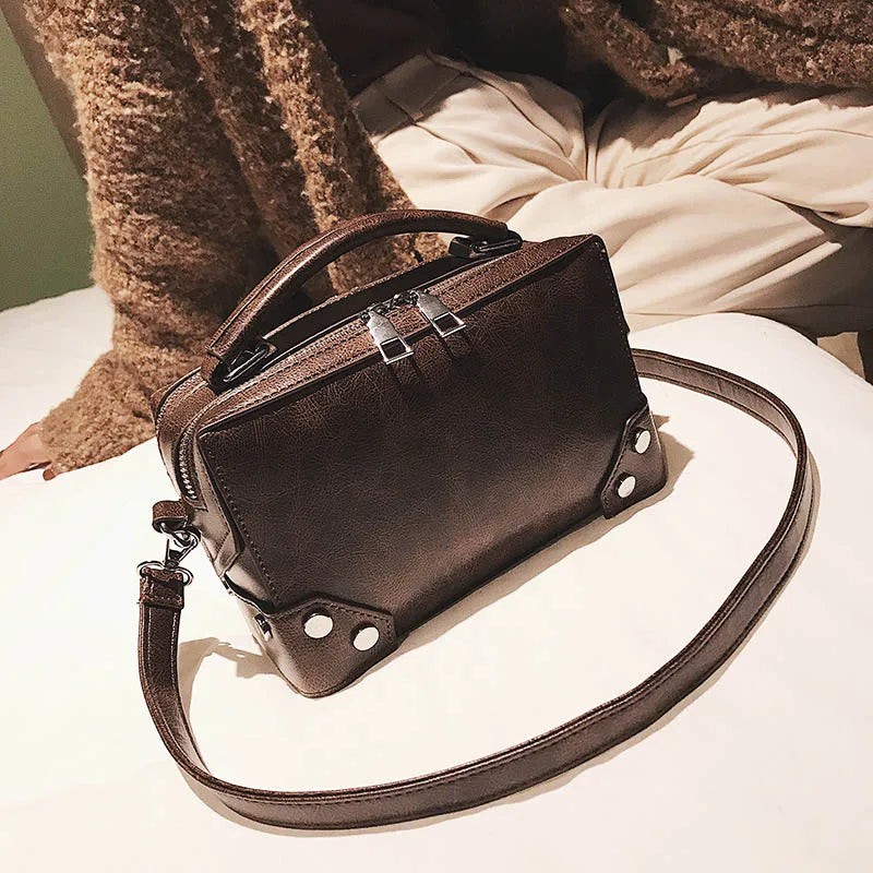 Borsa a tracolla in pelle marrone su letto, design elegante con manico superiore e dettagli metallici. Accessorio moda donna, stile casual chic.