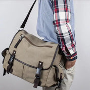 Uomo con camicia a quadri indossa borsa a tracolla in tela beige con fibbie marroni, ideale per lavoro o scuola. Stile casual e funzionale.