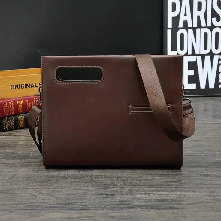 Borsa a tracolla in pelle marrone scuro su tavolo di legno, design elegante e moderno, ideale per uomo, con manico e tracolla regolabile.