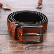 Cintura in pelle marrone con fibbia metallica rettangolare su sfondo in legno. Accessorio moda uomo elegante e di alta qualità.