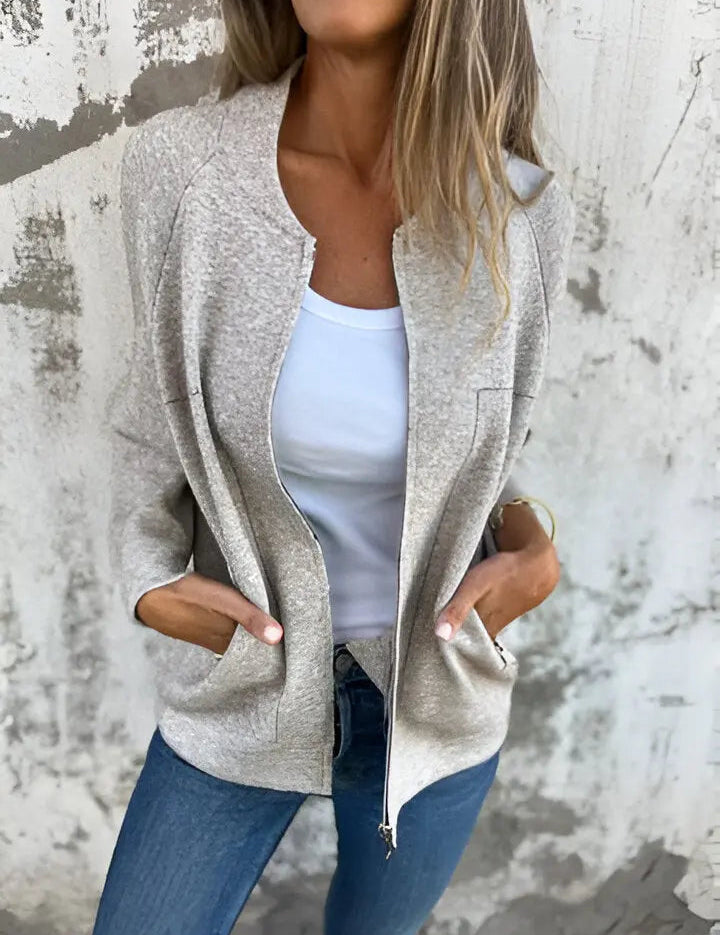 Giacca donna beige casual, tessuto morbido, con zip frontale e tasche, indossata su top bianco e jeans. Look moda autunno, stile urbano.