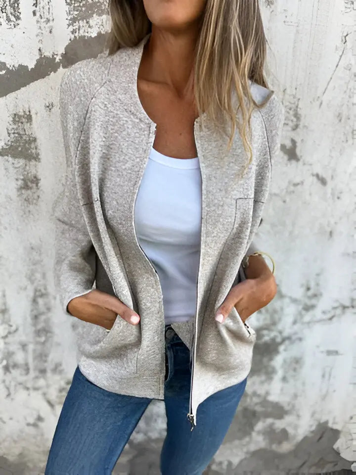 Giacca donna beige casual, tessuto morbido, con zip frontale e tasche, indossata su top bianco e jeans. Look moda autunno, stile urbano.