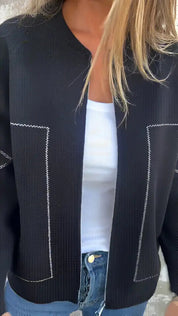 Giacca nera da donna con cuciture bianche a contrasto, indossata sopra una maglietta bianca. Moda casual, abbigliamento femminile elegante.