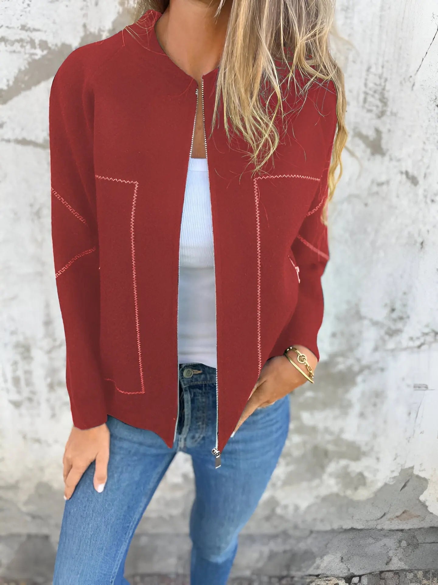 Giacca rossa donna, zip frontale, dettagli cuciture bianche, indossata con jeans blu e top bianco. Moda casual autunnale, stile urbano.