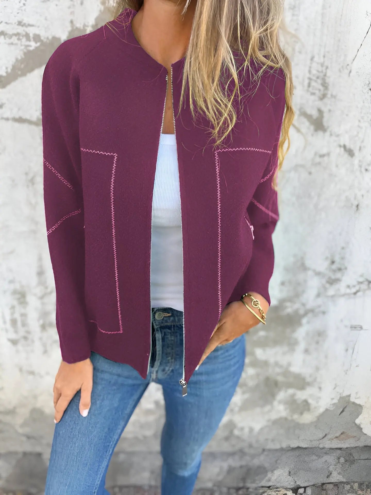 Donna con cardigan bordeaux aperto, top bianco e jeans blu. Moda casual autunnale, abbigliamento femminile elegante. Sfondo muro grigio.