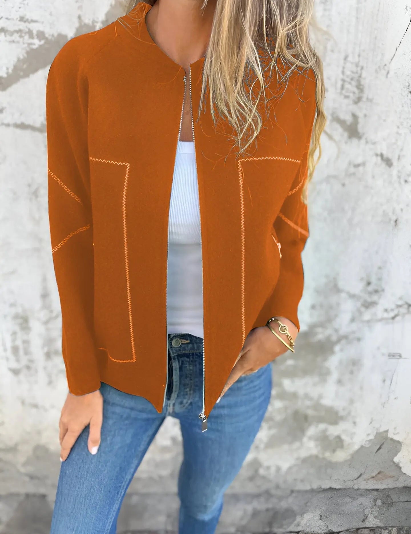 Donna con cardigan arancione aperto, top bianco e jeans blu. Moda autunnale casual, abbigliamento femminile trendy, stile urbano.