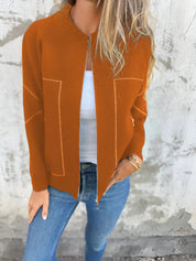 Donna con cardigan arancione aperto, top bianco e jeans blu. Moda autunnale casual, abbigliamento femminile trendy, stile urbano.
