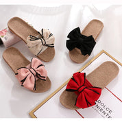Quattro paia di ciabatte estive in paglia con fiocco, colori beige, nero, rosa e rosso, su sfondo bianco. Scarpe donna moda estiva.