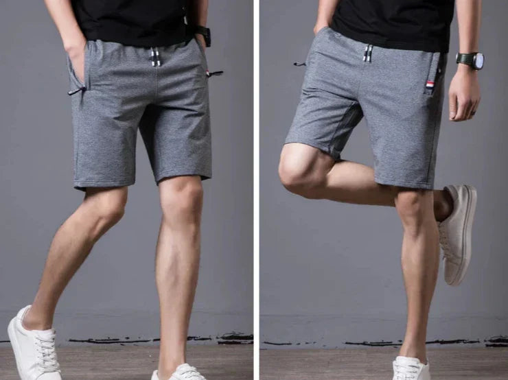 Shorts sportivi grigi da uomo, tessuto traspirante, elastico in vita, tasche laterali, abbinati a scarpe bianche casual.