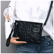 Borsa a tracolla nera in pelle con dettagli intrecciati, indossata da una persona in camicia bianca e jeans. Accessorio moda elegante e versatile.