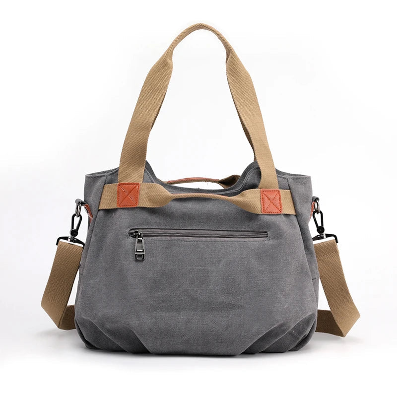 Borsa a tracolla in tela grigia con manici beige, tasca frontale con zip, dettagli in pelle marrone, ideale per moda casual e uso quotidiano.