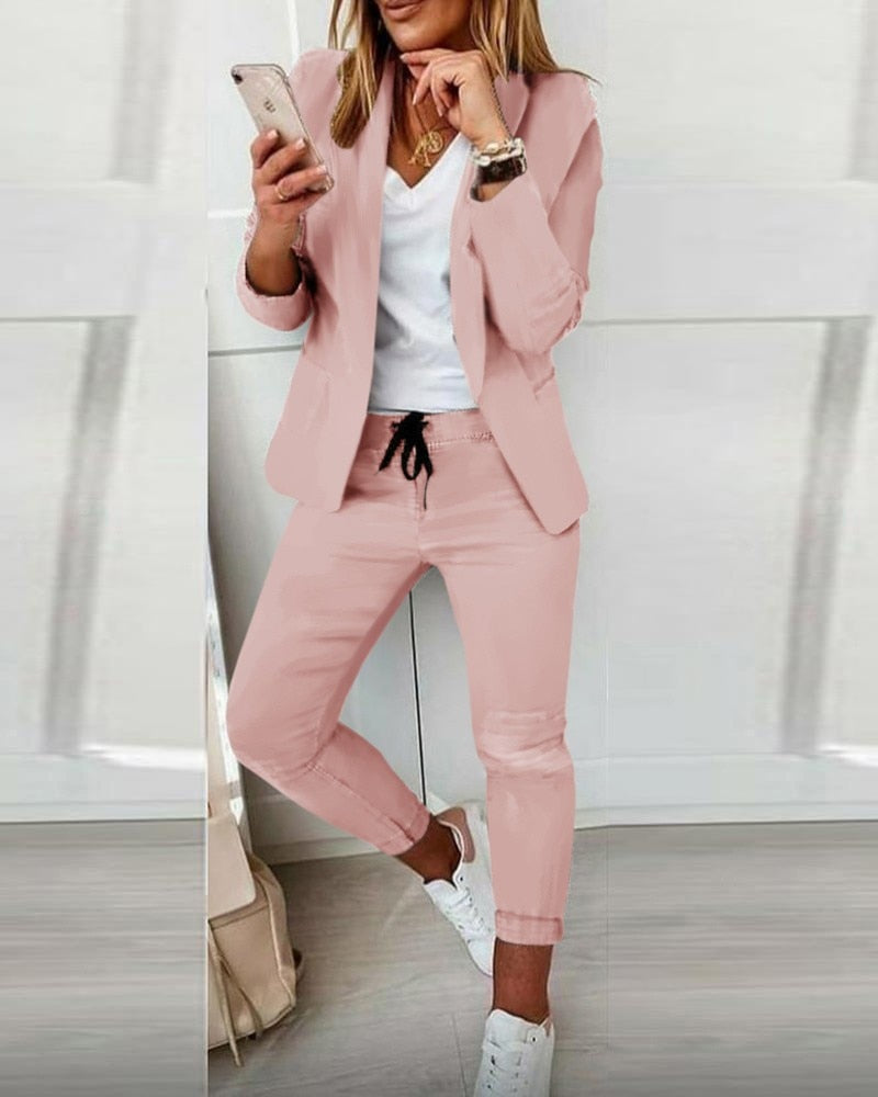 Donna in abito elegante rosa, giacca e pantaloni, con smartphone. Look casual-chic, moda femminile, abbigliamento trendy, scarpe bianche.