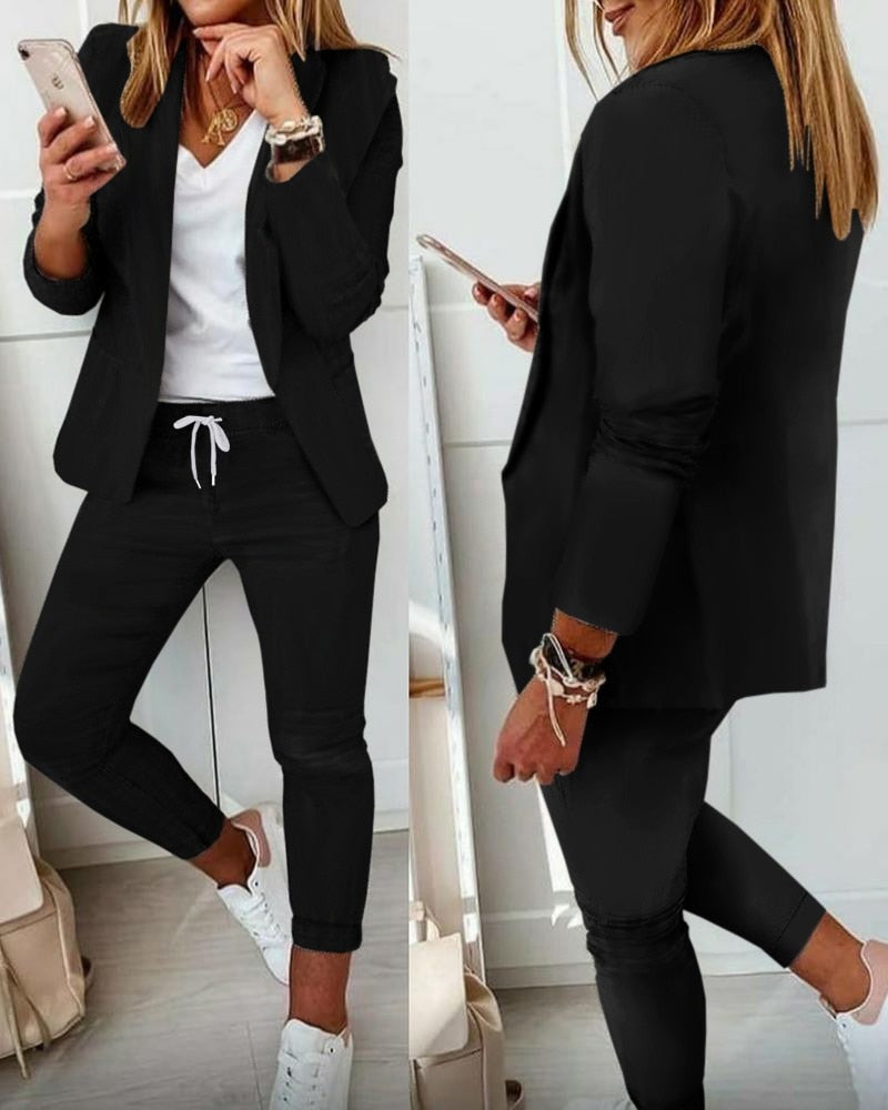 Donna in abbigliamento casual elegante: blazer nero, pantaloni sportivi neri, t-shirt bianca, sneakers bianche. Outfit moda donna autunno.