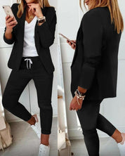 Donna in abbigliamento casual elegante: blazer nero, pantaloni sportivi neri, t-shirt bianca, sneakers bianche. Outfit moda donna autunno.