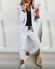 Donna in abbigliamento casual elegante: blazer bianco, t-shirt nera, pantaloni bianchi, sneakers bianche. Outfit moderno e alla moda.
