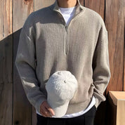 Uomo con maglione beige a collo alto e zip, tiene un cappello bianco. Sfondo in legno. Moda casual autunnale, abbigliamento maschile elegante.