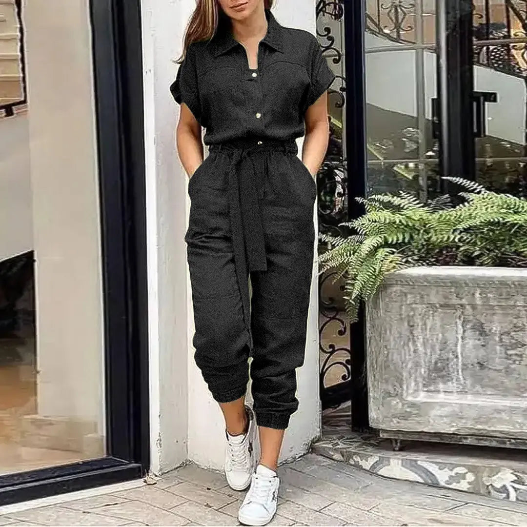 Tuta nera elegante da donna con cintura, maniche corte e pantaloni a coste, abbinata a sneakers bianche. Look casual chic per ogni occasione.