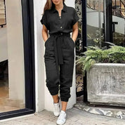 Tuta nera elegante da donna con cintura, maniche corte e pantaloni a coste, abbinata a sneakers bianche. Look casual chic per ogni occasione.