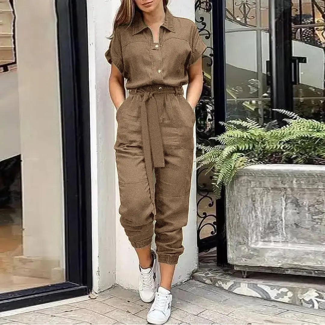 Tuta jumpsuit marrone da donna con cintura, maniche corte, abbinata a sneakers bianche. Look casual chic per moda urbana.