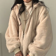 Giacca in pelliccia sintetica beige, donna, con cappuccio e zip, indossata su maglione a collo alto. Moda invernale elegante e calda.