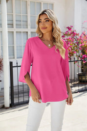 Donna con maglia rosa a maniche lunghe, pantaloni bianchi, collana, sfondo con fiori e finestra. Moda femminile, abbigliamento casual elegante.