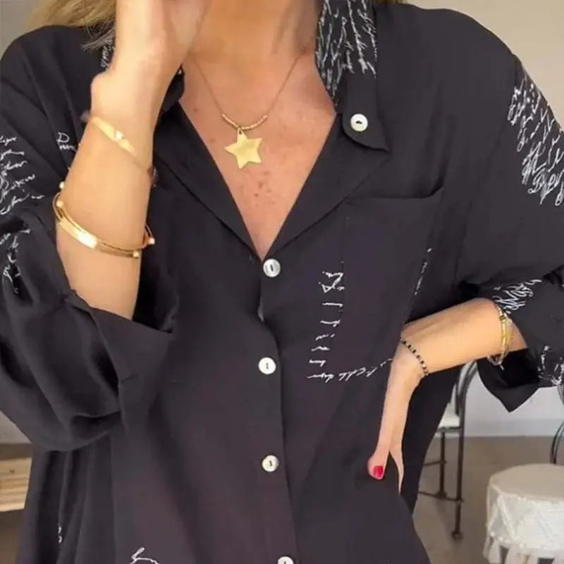 Camicia nera da donna con scritte bianche, maniche lunghe, colletto classico, abbinata a collana con ciondolo a stella e bracciali dorati.