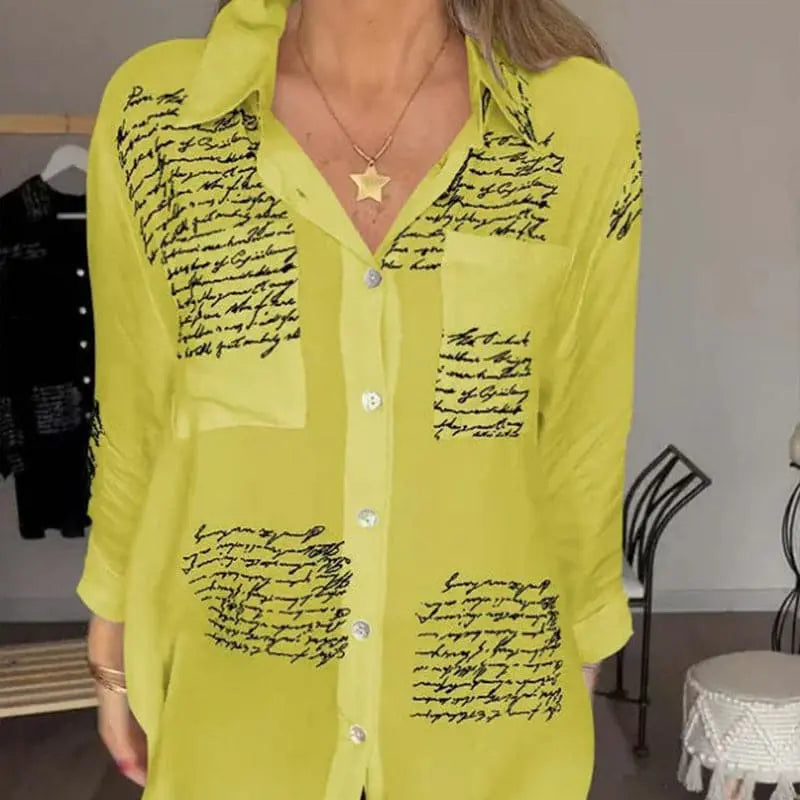 Camicia donna gialla con scritte nere, maniche lunghe, colletto classico, bottoni frontali, tasca sul petto, stile casual elegante.