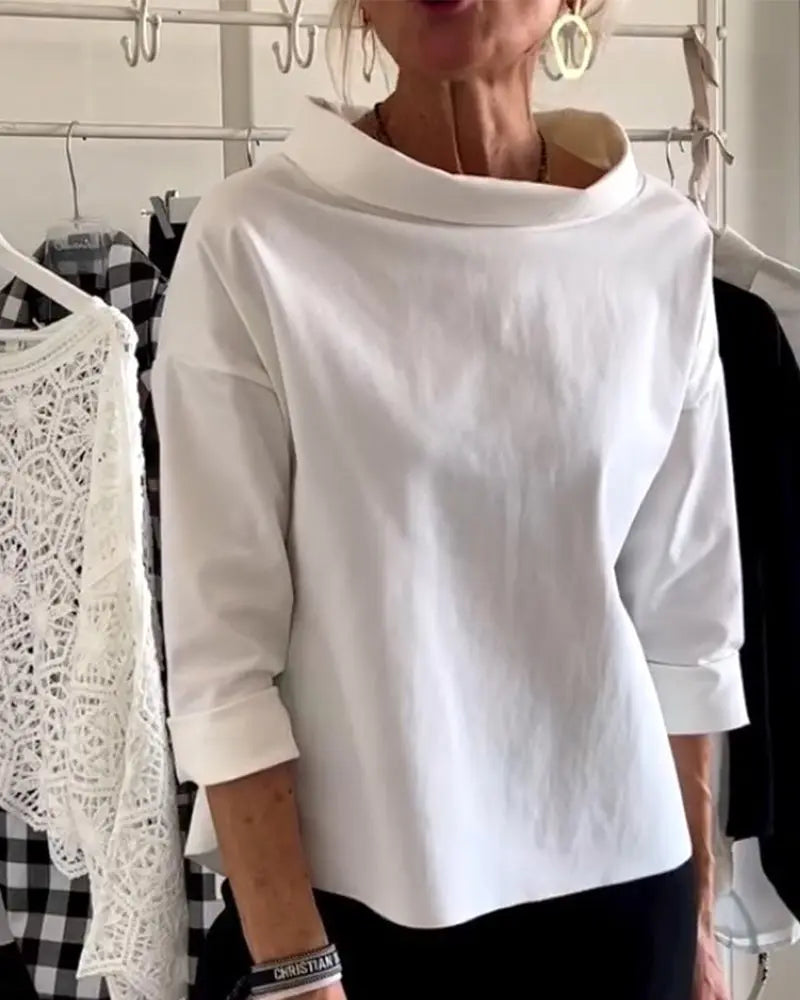 Blusa bianca elegante con collo ampio, maniche a tre quarti, indossata da una donna. Sfondo con abiti appesi, moda femminile, stile casual chic.