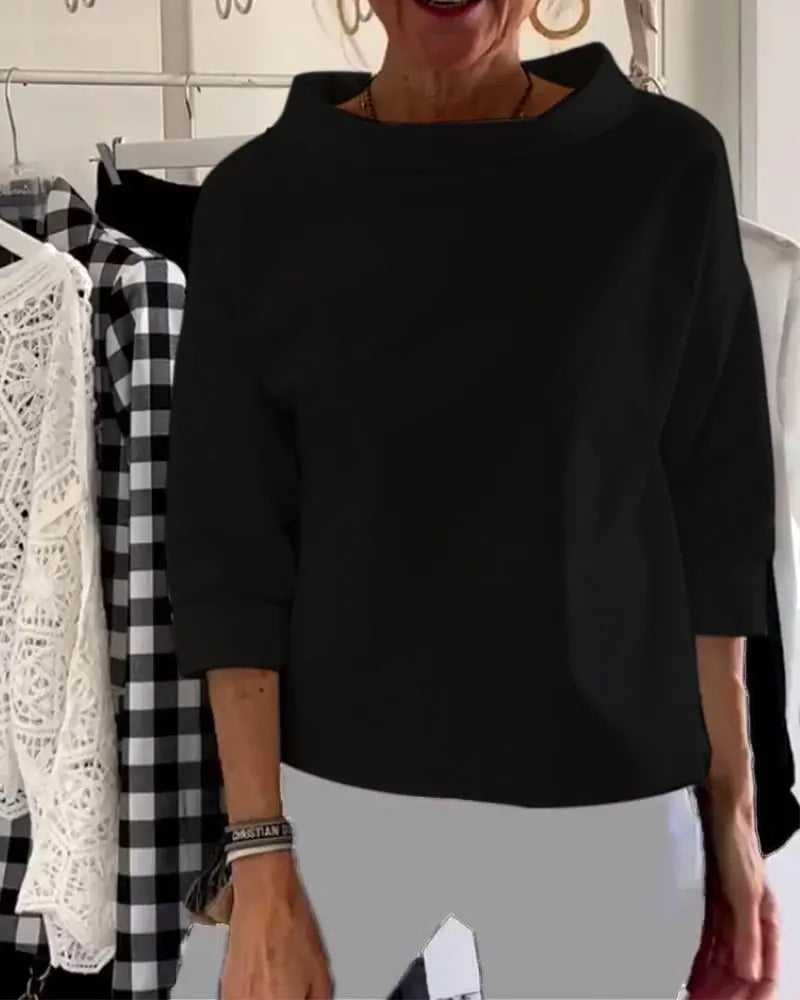 Donna indossa maglia nera a maniche lunghe, sfondo con abiti appesi. Moda femminile, abbigliamento casual elegante, tendenze autunno-inverno.