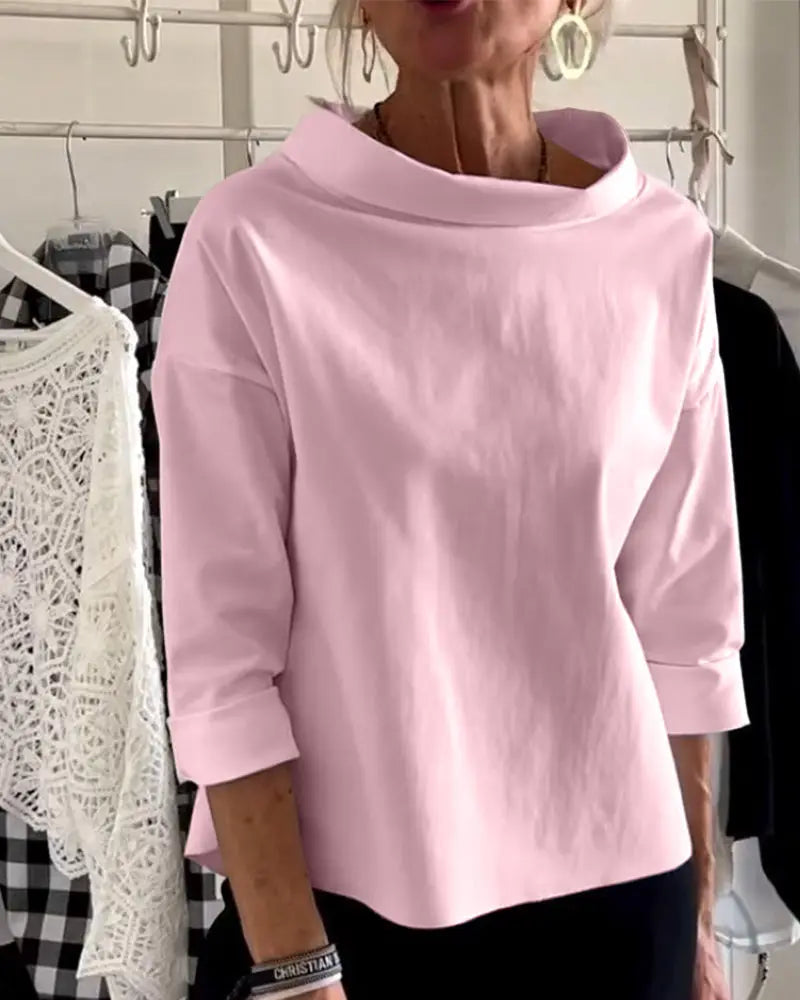 Donna indossa maglia rosa a maniche lunghe con collo ampio, accanto a vestiti appesi. Moda femminile, abbigliamento casual elegante.