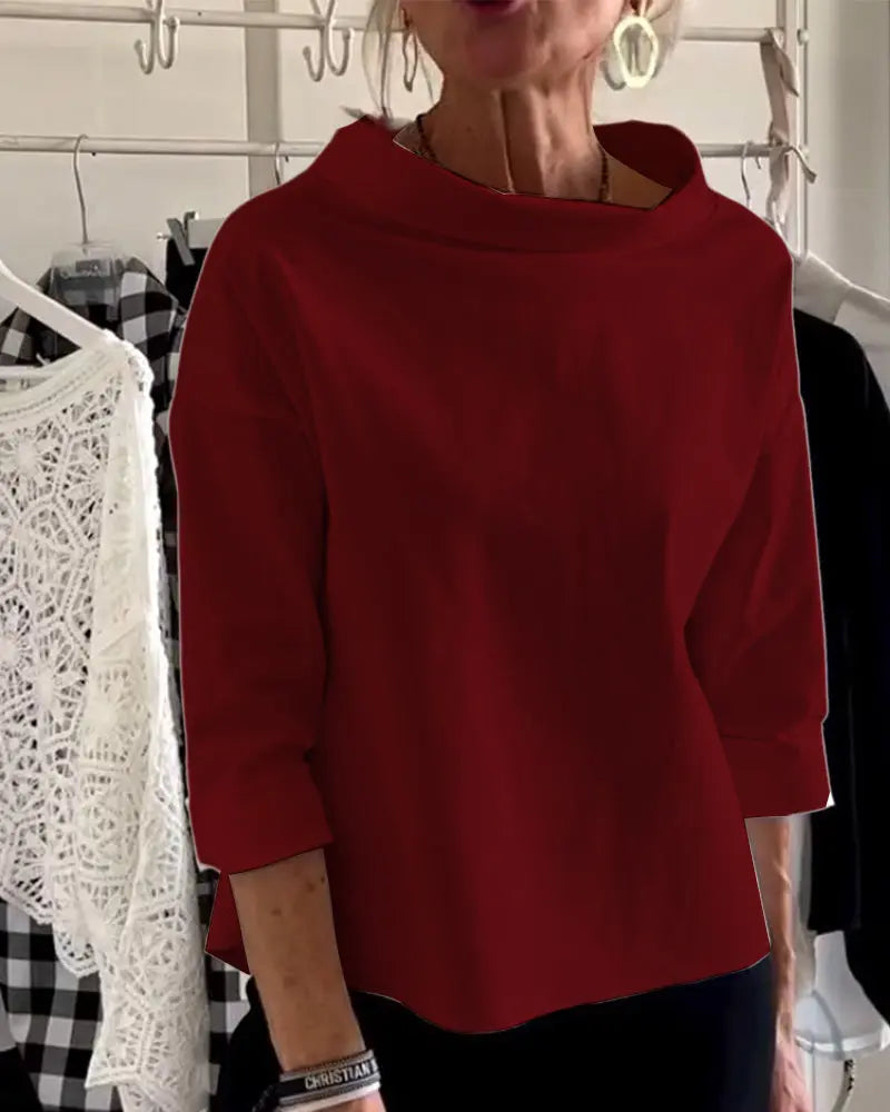 Maglia rossa a maniche lunghe, collo alto, indossata da una donna. Sfondo con abiti appesi. Moda femminile elegante, abbigliamento casual chic.