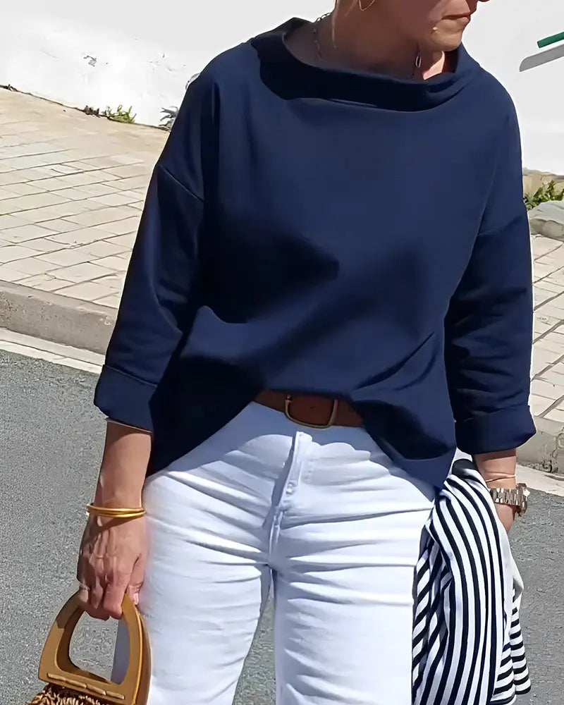 Donna con maglia blu scuro, pantaloni bianchi, borsa in legno e giacca a righe. Moda casual elegante, abbigliamento primaverile estivo.
