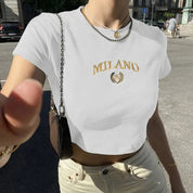 Donna con t-shirt bianca "Milano", collana dorata, borsa a tracolla nera, jeans chiari, in strada soleggiata. Moda estiva urbana, stile casual.