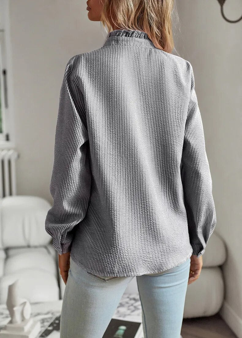 Camicia donna a righe grigie, maniche lunghe, collo alto, tessuto a trama, indossata con jeans chiari. Moda casual autunnale.