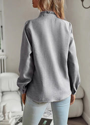 Camicia donna a righe grigie, maniche lunghe, collo alto, tessuto a trama, indossata con jeans chiari. Moda casual autunnale.