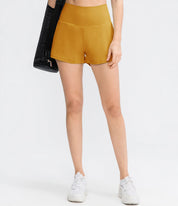 Shorts sportivi donna gialli, vita alta, tessuto elasticizzato, ideali per fitness e yoga. Modello con borsa nera e scarpe bianche.