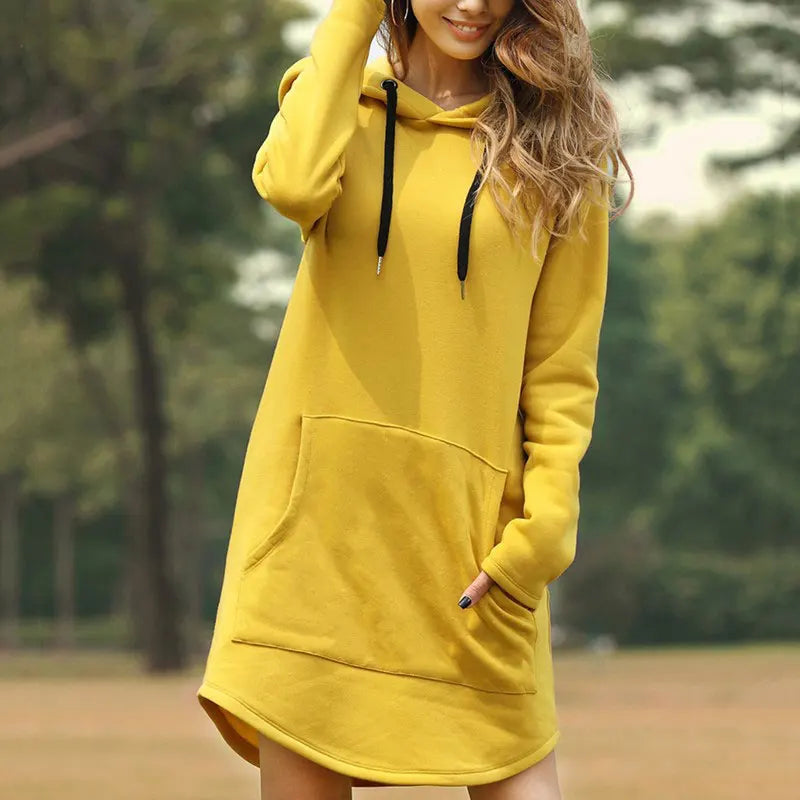 Donna con felpa gialla con cappuccio, tasca frontale e lacci neri, in un parco. Moda casual autunnale, abbigliamento comodo e trendy.