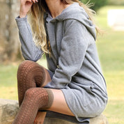 Donna seduta su una roccia indossa un abito felpa grigio con cappuccio e calze lunghe marroni. Moda casual autunnale, abbigliamento comodo.