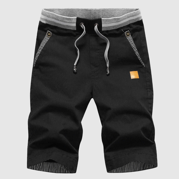 Pantaloncini neri da uomo con coulisse, tasche con zip, dettagli a righe, e bordo grigio. Ideali per sport e tempo libero. Moda casual estiva.