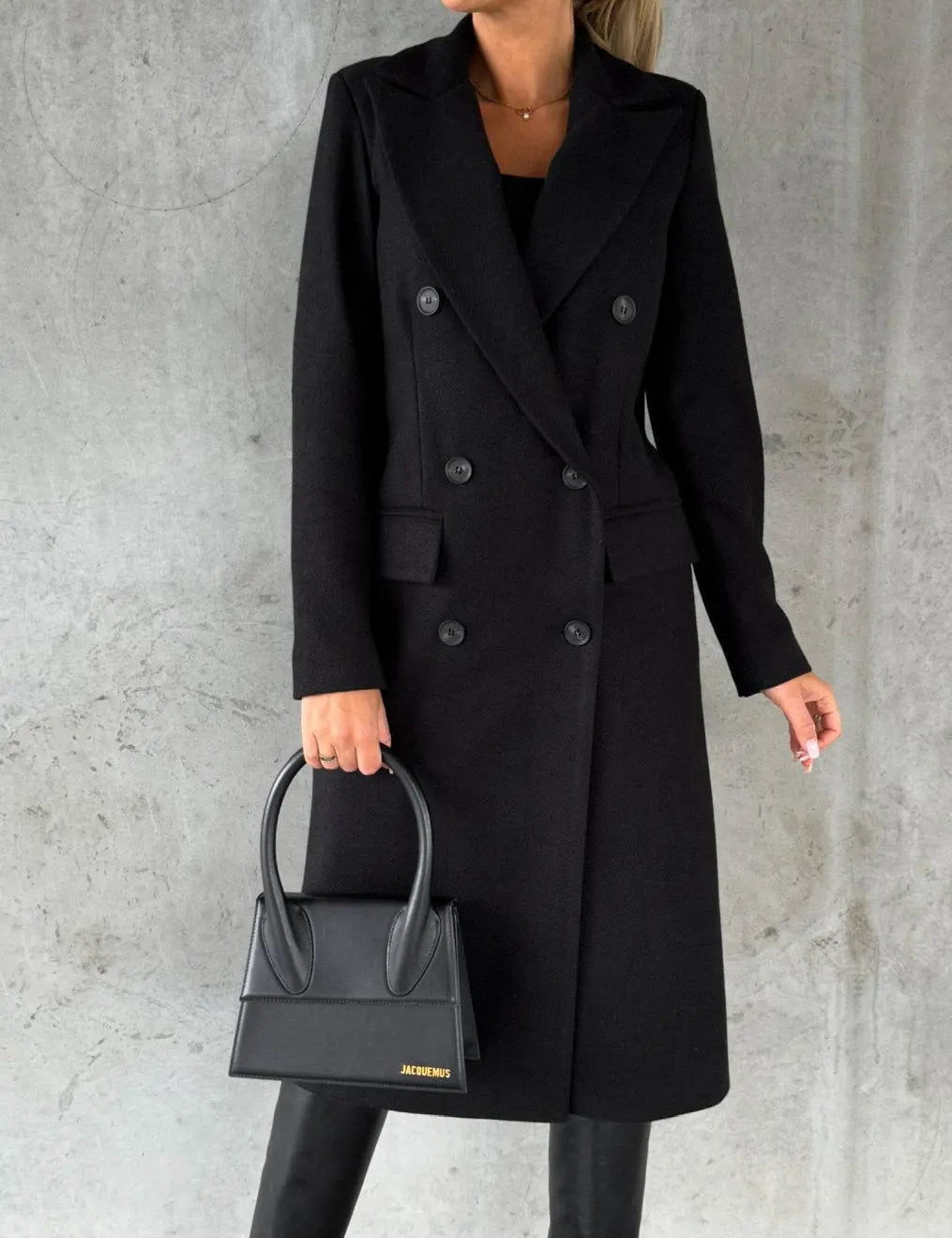 Cappotto nero elegante donna, doppio petto, abbinato a borsa nera di design, moda autunno inverno, stile sofisticato e moderno.