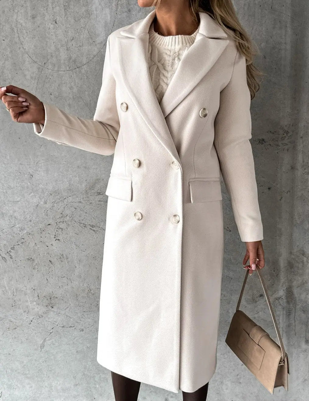 Cappotto lungo donna beige elegante, doppio petto, abbinato a borsa a mano marrone chiaro, su sfondo grigio. Moda autunno inverno.