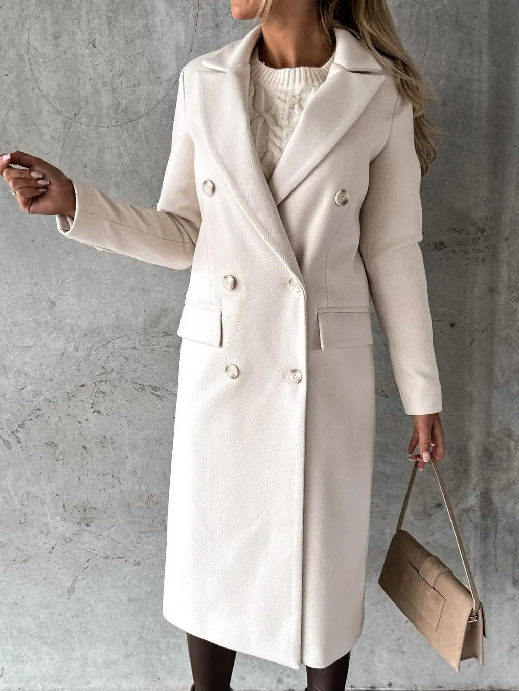 Cappotto lungo donna beige elegante, doppio petto, abbinato a borsa a mano marrone chiaro, su sfondo grigio. Moda autunno inverno.