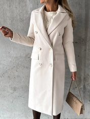 Cappotto lungo donna beige elegante, doppio petto, abbinato a borsa a mano marrone chiaro, su sfondo grigio. Moda autunno inverno.